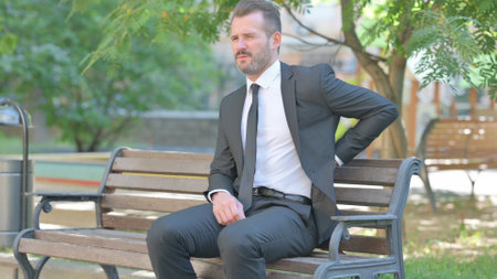 Young Businessman with Back Pain Sitting Outdoorの写真素材