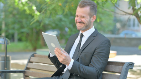Young Businessman Celebrating Success on Tablet while Sitting Outdoorの写真素材
