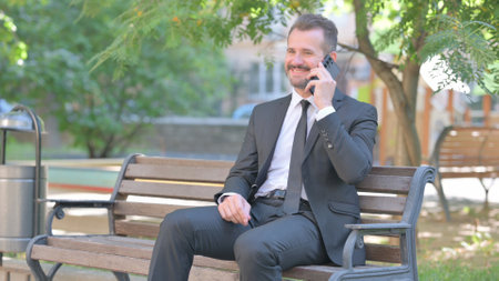 Young Businessman Talking on phone while Sitting Outdoorの写真素材