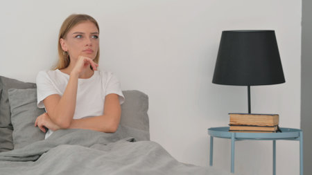 Pensive Young Woman Sitting in Bedの写真素材