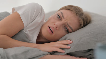 Close up of Uncomfortable Young Woman Having Nightmare while Sleeping on Side in Bedの写真素材