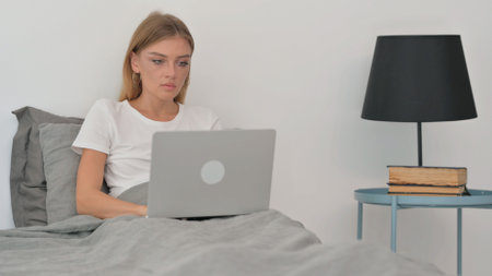 Young Woman Working on Laptop while Sitting in Bedの写真素材