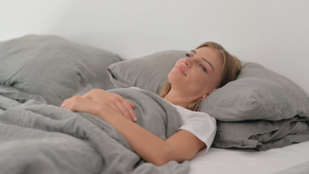 Pensive Young Woman Lying in Bedの写真素材