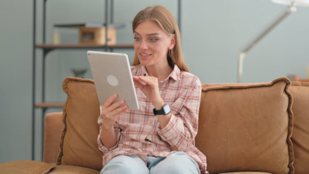 Young Woman Doing Video Chat on Tablet while Sitting on Sofa at Homeの写真素材