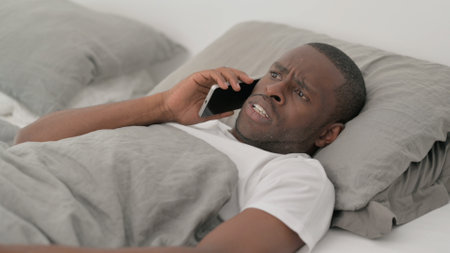 Angry Man Talking on Phone while Lying in Bedの写真素材