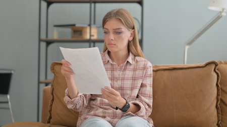 Young Woman Doing Paperwork while Sitting on Sofa at Homeの写真素材