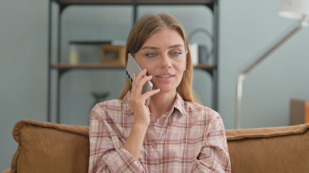Young Woman Talking on phone while Sitting on Sofa at Homeの写真素材