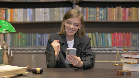 Female Lawyer Celebrating Success on Phone in Officeの写真素材
