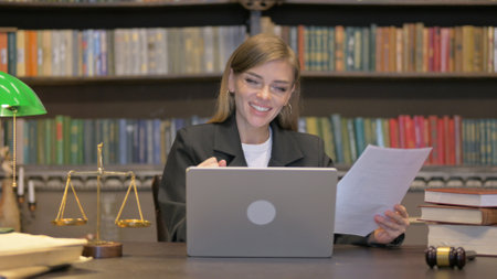 Cheering Female Lawyer Doing Paperwork on Laptop in Officeの写真素材