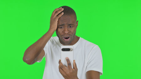 Portrait of African Man Shocked by Loss on Phone on Green Backgroundの写真素材