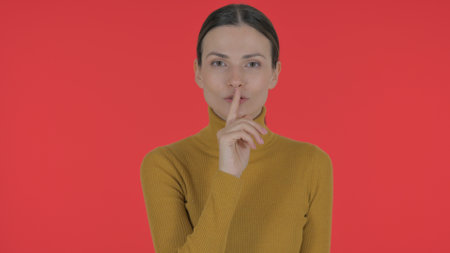Casual Young Woman with Silence Gesture on Red Background, Portraitの写真素材