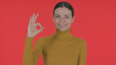 Casual Young Woman with Okay Sign on Red Background, Portraitの写真素材