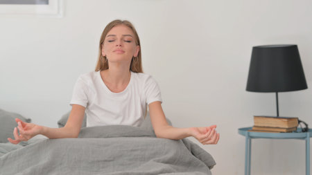 Young Woman Doing Yoga while Sitting on Bedの写真素材