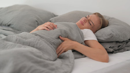 Young Woman with Back Pain while Sleeping in Bedの写真素材
