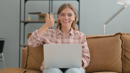 Thumbs Up by Young Woman Using Laptop Indoor on Sofaの写真素材