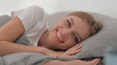 Close up of Smiling Young Woman Lying on Side in Bedの写真素材