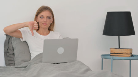 Young Woman in Denial Looking at Camera while in Bed with Laptopの写真素材