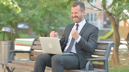 Young Businessman Celebrating Success on Laptop Outdoorの写真素材