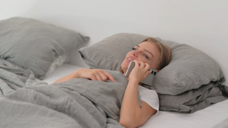 Young Woman Talking on phone while Lying in Bedの写真素材