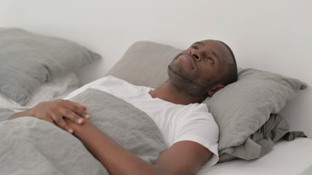 Pensive African Man Lying in Bedの写真素材