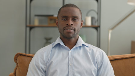 Portrait of Serious African Man Sitting on Sofa at Homeの写真素材