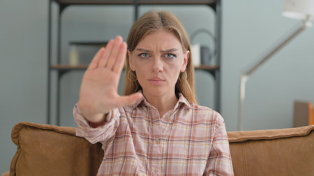 Stop Gesture by Young Woman Sitting on Sofa at Homeの写真素材