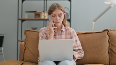 Young Woman Talking on phone while Using Laptop Outdoorの写真素材