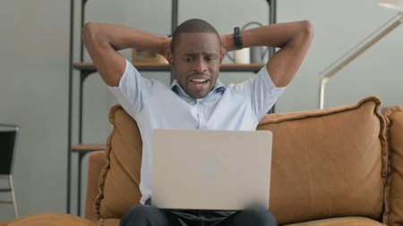 African Man Shocked by Loss on Laptop while Sitting on Sofaの写真素材