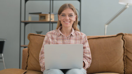 Approval Gesture by Young Woman Using Laptop while Sitting on Sofaの写真素材