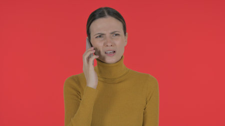 Angry Casual Young Woman Talking on Phone on Red Background, Portraitの写真素材