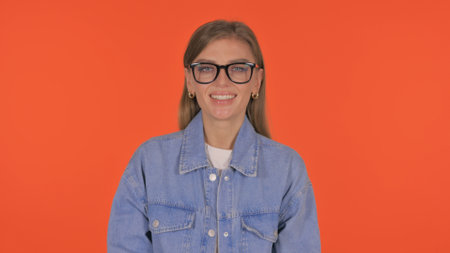 Casual Young Woman Shaking Head in Acceptance on Orange Background, Portraitの写真素材