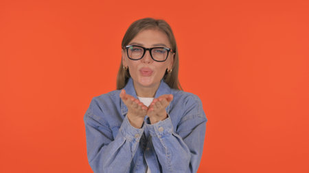 Casual Young Woman Blowing Flying Kiss on Orange Backgroundの写真素材