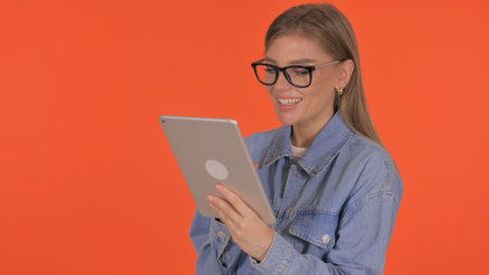 Casual Young Woman Doing Video Chat on Tablet on Orange Backgroundの写真素材