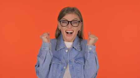 Casual Young Woman Celebrating Success on Orange Background, Portraitの写真素材