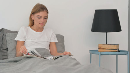 Young Woman Reading Book while Sitting in Bedの写真素材