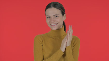 Casual Young Woman Clapping for Team on Red Background, Portraitの写真素材