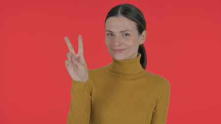 Casual Young Woman with Victory Sign on Red Background, Portraitの写真素材