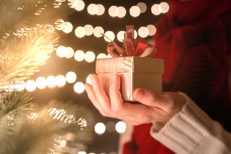 Hand of female holding Christmas gift box on bokeh lights background.の写真素材