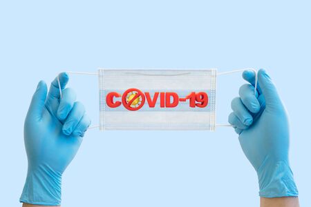 Doctor hands holding surgical mask with covid-19 word and stop sign on light blue background for stop coronavirus spread concept.の写真素材
