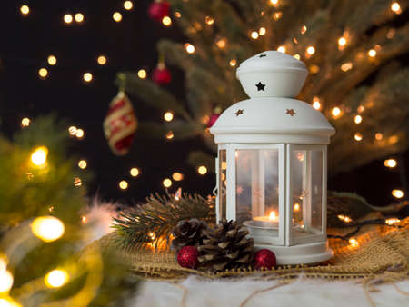 Candle in christmas lantern with fir branch, pine cones and baubles with blurred decorated christmas tree and bokeh lights background.の写真素材