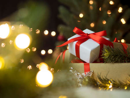 Stack gift box with fir branches in blurry christmas tree in background.の写真素材