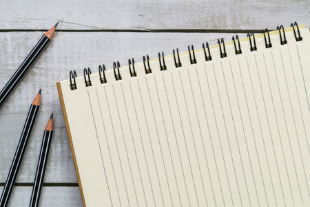 Top view of blank notebook and pencils on white wood table