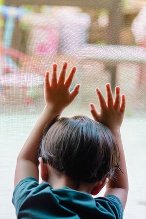 One boy placed both hands on a mosquito net. He wants to go play outside. But the situation outside of the epidemic Causing him to stay in the house for safetyの写真素材