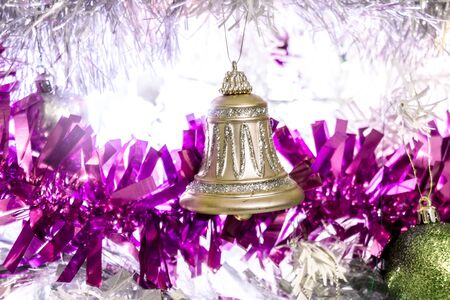 A gold glittery bell on w white christmas tree covered in purple tinsilの写真素材