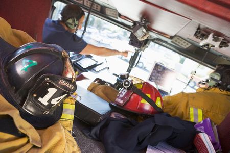 Two firefighters driving a fire engine with gear in the back (selective focus)の写真素材