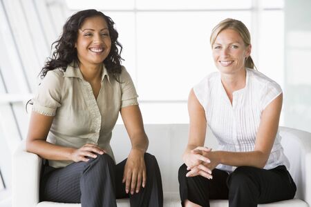 Two businesswomen sitting indoors smiling (high key/selective focus)の写真素材