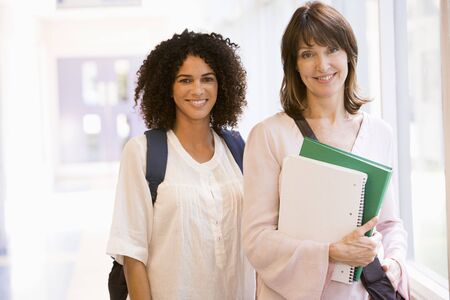 Two women standing in corridor with books (high key)の写真素材