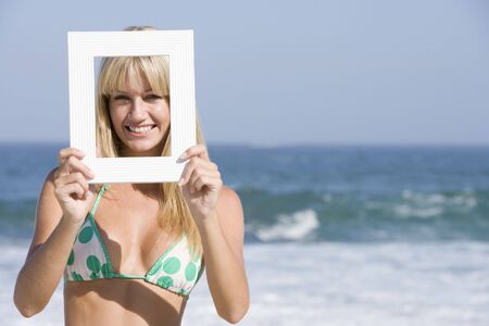 Woman on a beach holding a frame to her faceの写真素材