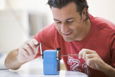 Man indoors using pencil sharpener smilingの写真素材