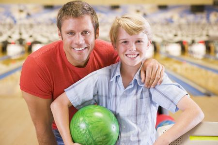 Man and young boy in bowling alley holding ball and smilingの写真素材